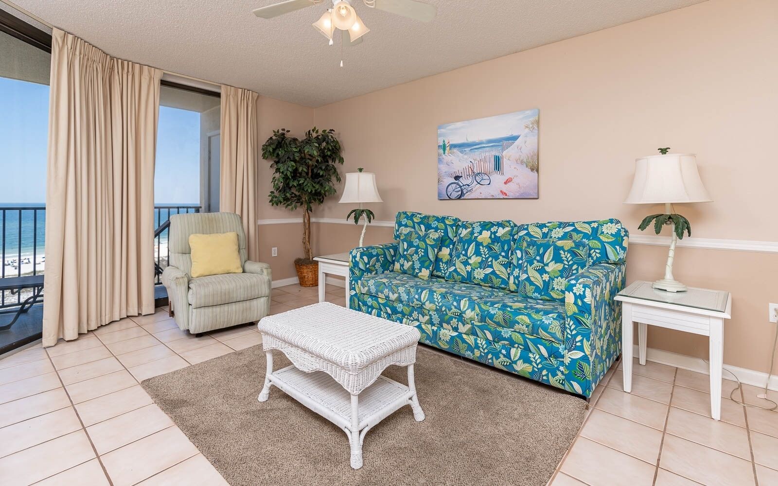 Ein Wohnzimmer mit einer Couch, einem Sessel und einem kleinen Tisch. Durch das Fenster hat man Blick auf den Strand.