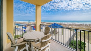 A balcony with a table and chairs, overlooking a beach with umbrellas and lounge chairs. - Phoenix V 103 | Spacious Coastal Retreat (Orange Beach)