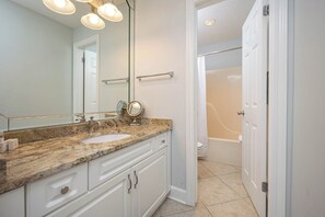 A bathroom with a marble sink, a large mirror, and a bathtub visible through an open door. - Three Bedroom ~ Phoenix VII ~ Comes with Parking! (Orange Beach)