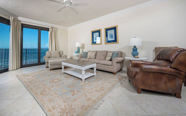 A spacious living room with a large window overlooking the ocean, a beige sofa, a coffee table, and a leather armchair. - Three Bedroom ~ Phoenix VII ~ Comes with Parking! (Orange Beach)