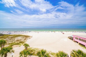 Ein Strand mit einem rosafarbenen Gebäude, Palmen und blauem Himmel.