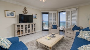 A living room with a television, two sofas, a coffee table, and a view of the sea through large windows.