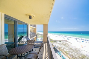 A balcony with a table and chairs, overlooking a beach with umbrellas and lounge chairs.