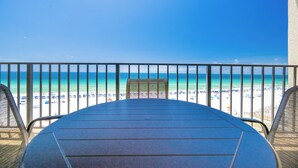 Vista desde un balcón con vistas a una playa, con una mesa y sillas al frente.