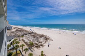 Blick auf einen Strand vom Balkon aus, mit blauem Himmel, Sandstrand und einigen Personen.