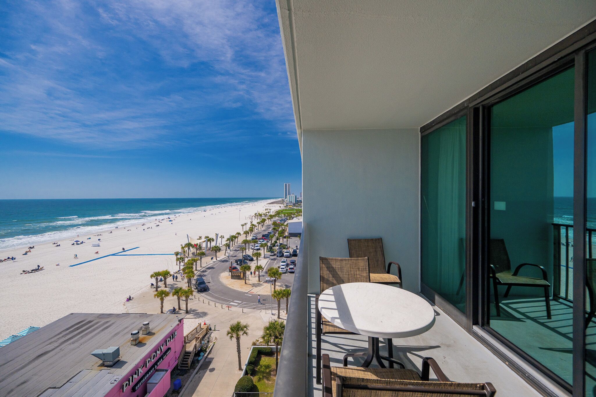 A balcony with a view of a beach, a table, and chairs.