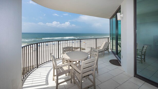 A balcony with a view of the ocean, a round table with chairs, and a glass door leading to a room.