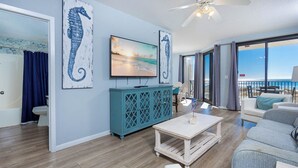 Una sala de estar con televisión, un mueble azul turquesa y vista al océano.