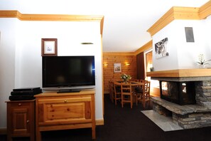 A wooden entertainment center with a flat-screen TV, a fireplace, and a dining area with wooden furniture. - Superb duplex in luxury apartment at foot of slopes (Val-D'isère)