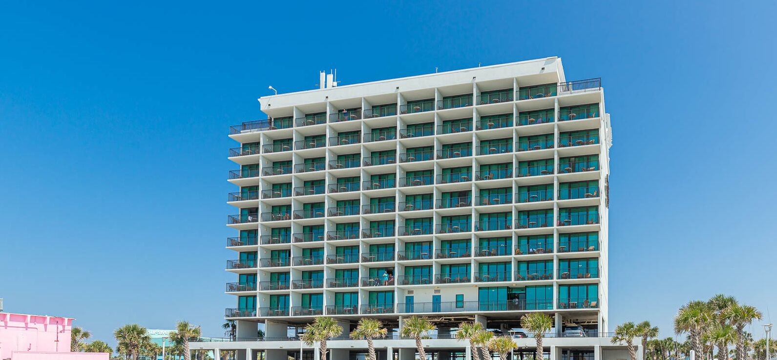 Un hotel de varios pisos con balcones, techo plano y un cielo azul despejado.