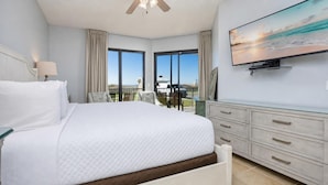 A bedroom with a large bed, a TV, a balcony with a view, and a ceiling fan.