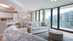A spacious living room with a sofa, a coffee table, and a view of a balcony with buildings.