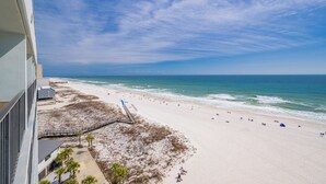 Une vue sur la plage depuis un balcon, avec un ciel dégagé, une plage de sable et l’océan.