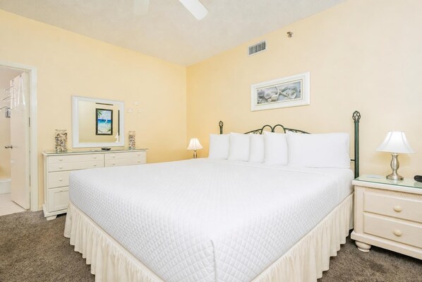 A bedroom with a large bed, a dresser, a nightstand, a lamp, and a framed picture on the wall.