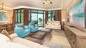 Ein geräumiges Wohnzimmer mit großem Fernseher, bequemen Sitzmöglichkeiten, einem Deckenventilator und einem Balkon mit Blick.