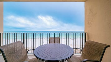 A balcony with a view of the beach, a round table, and two chairs.
