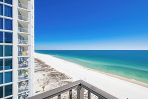 Un hotel frente a la playa con balcones que dan a una playa de arena y aguas azul turquesa.