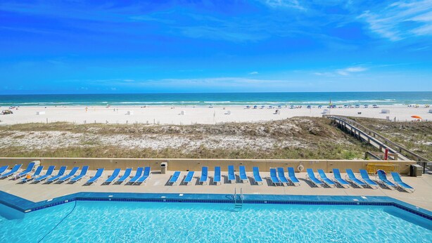A pool with lounge chairs, a beach in the background, and a clear sky. - PREMIUM 2 Bedroom @ P5 ~ Great Rates (Orange Beach)