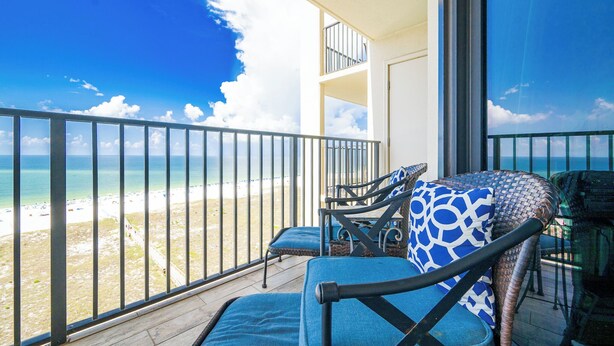 A balcony with a view of the beach, two chairs with blue cushions, and a table with a glass top. - Phoenix VII Two Bedroom Condo ~ GULF FRONT (Orange Beach)