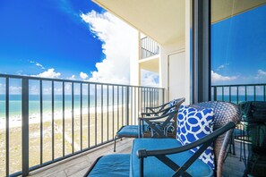 Un balcon donnant sur la plage, deux chaises avec des coussins bleus et une table avec un plateau en verre.