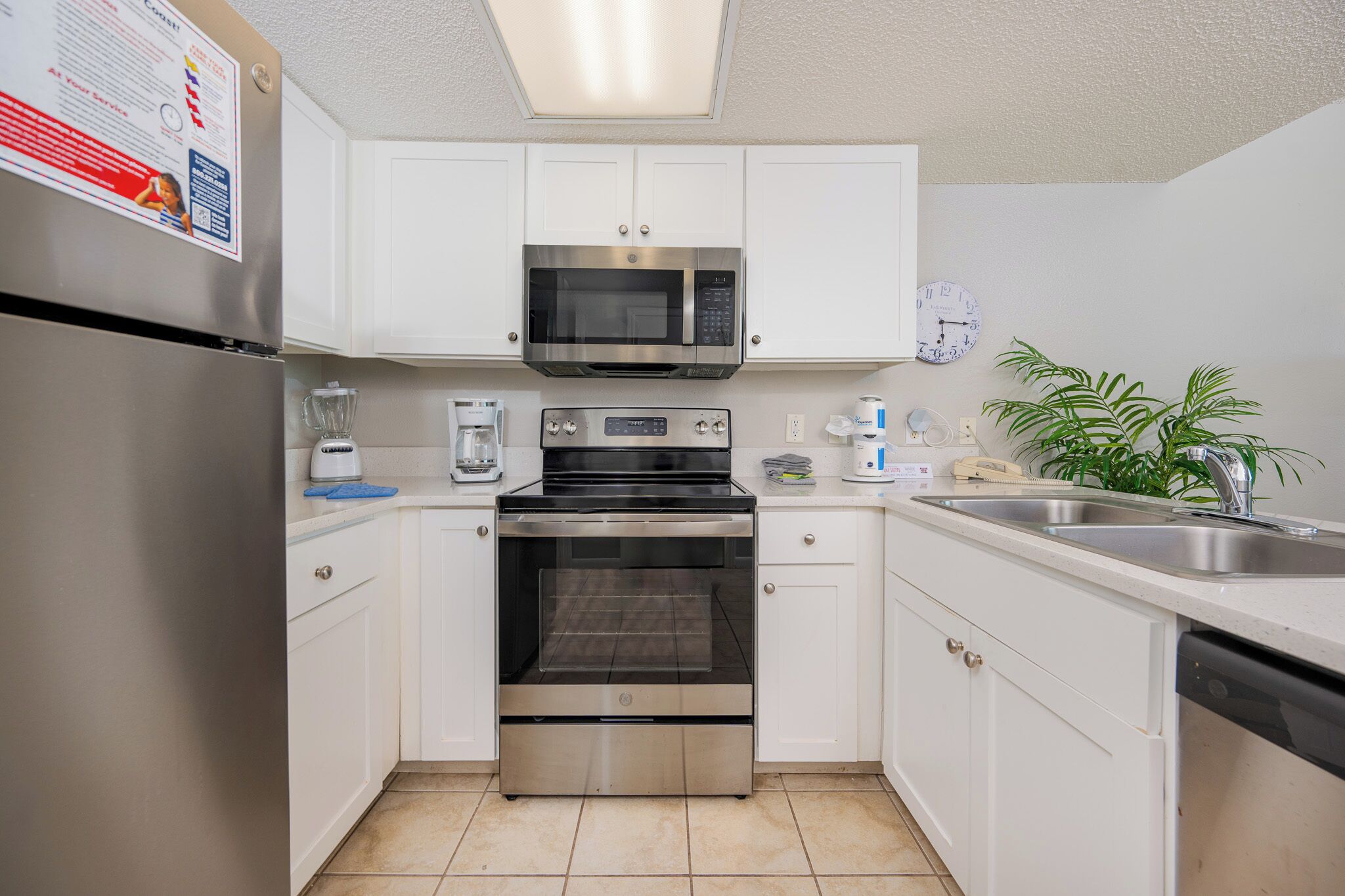 Una cocina compacta con armarios blancos, un refrigerador de acero inoxidable, un microondas, un horno, un lavaplatos y una cafetera.