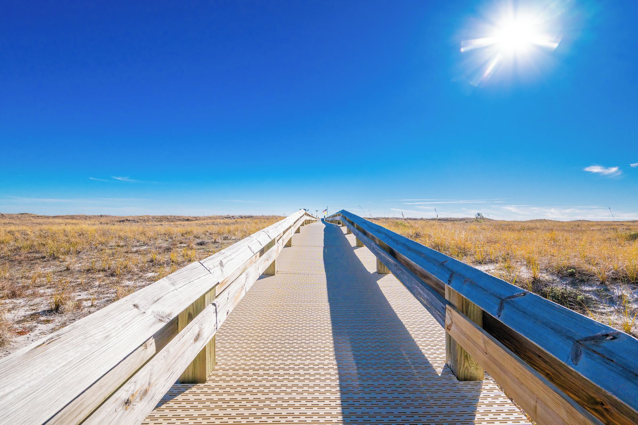 Stroll along the boardwalk leading to the beach, surrounded by golden grasses and a bright blue sky above at Phoenix VII