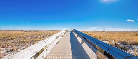 Stroll along the boardwalk leading to the beach, surrounded by golden grasses and a bright blue sky above at Phoenix VII