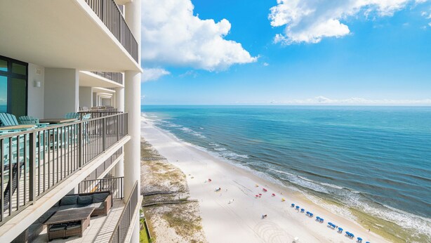 A beachfront hotel with a balcony overlooking the ocean, a sandy beach, and a clear sky. - The Oasis at Orange Beach, formerly known as Phoenix West II, Unit 2204 (Orange Beach)