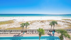 A poolside view overlooking a beach with lounge chairs and palm trees. - The Oasis at Orange Beach, formerly known as Phoenix West II, Unit 303 (Orange Beach)