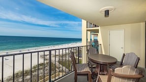 Ein Balkon mit Tisch und Stühlen, der auf einen Strand mit einem Holzsteg und Blick auf das Meer blickt.