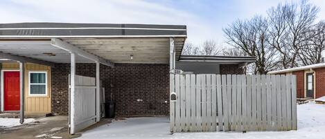Un garage attenant à une maison, avec un mur en briques, une porte rouge et une clôture blanche.