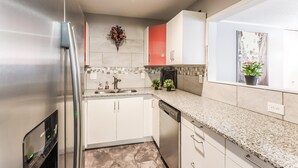 Una cocina moderna con armarios blancos, encimera de granito, refrigerador de acero inoxidable y lavavajillas.