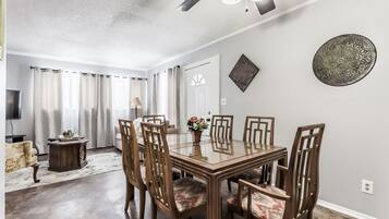 A dining area with a glass-top table and six wooden chairs, a chandelier, and a decorative wall piece.