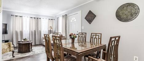 A dining area with a glass-top table and six wooden chairs, a chandelier, and a decorative wall piece.