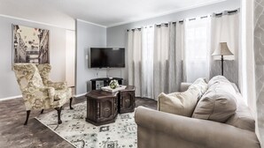 Una sala de estar con sofá, sillón, televisor y un mueble decorativo.