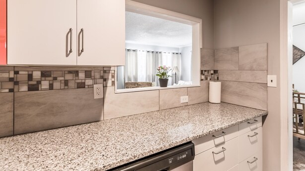 Una cocina moderna con encimeras de granito, lavavajillas y ventana con vistas al baño.