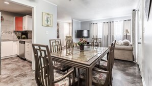 Una sala de estar moderna con una mesa de comedor de cristal, sillas de madera, un sofá y un televisor montado en la pared.