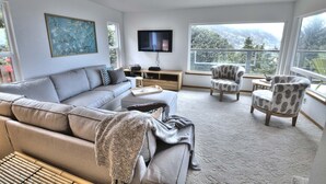 Un salón amplio con un gran ventanal, un televisor de pantalla plana, un sofá y dos sillones estampados.