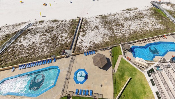 Vue aérienne d’un complexe hôtelier doté de deux piscines, d’une plage et d’une promenade en bord de mer.
