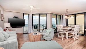 Ein geräumiges Wohnzimmer mit einem Flachbildfernseher, einem Deckenventilator, einem runden Couchtisch und einem Essbereich mit weißen Stühlen und einem Holztisch.