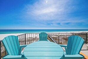 Vista desde una terraza con dos sillas Adirondack turquesas mirando a la playa.