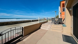 A balcony with a view of the ocean, a table and chairs, and a building with an orange facade.