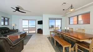 A spacious living room with a large wooden dining table, a sofa, and a ceiling fan.
