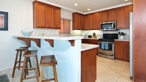 A kitchen with wooden cabinets, a central island with stools, a microwave, and a stove.