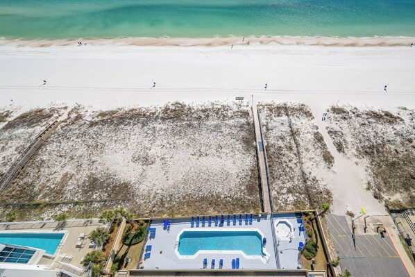 Vue aérienne d’un complexe hôtelier en bord de mer, avec une piscine, un accès à la plage et une promenade en bord de mer.