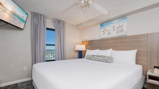 Ein Hotelzimmer mit einem großen Bett, einem Deckenventilator, einem Gemälde, einem Nachttisch und Blick ins Freie.