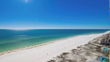 A beach with clear blue water, sandy shore, and buildings with pools.
