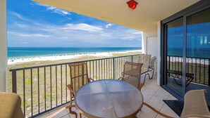 Un balcon avec une table et des chaises, donnant sur une plage sous un ciel dégagé.