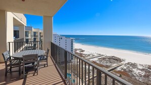 A balcony with a table and chairs, overlooking a beach with a clear blue sky. - AMAZING VIEWS! Top floor two bedroom at Phoenix 7 (Orange Beach)