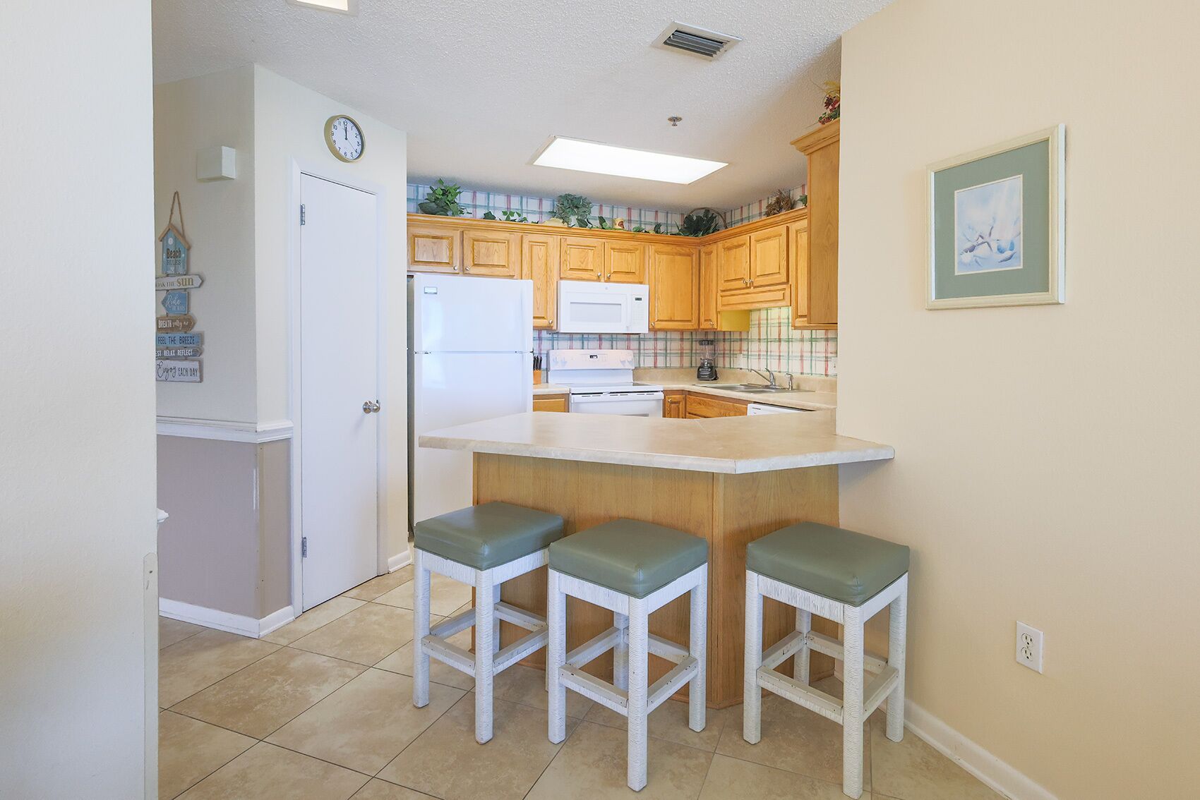 A kitchen with wooden cabinets, a white refrigerator, a sink, and a bar area with stools.